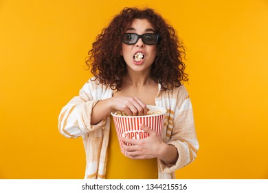 Image of a cute shocked beautiful young curly girl posing isolated over yellow wall background wearing glasses eat popcorn watch film.