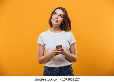 Image Of Cute Thinking Young Woman Standing Isolated Over Yellow Background Chatting By Mobile Phone. Looking Aside.