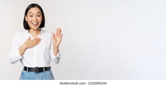 Image of cute young female office worker, asian girl student raising hand up and put palm on chest, name herself, introduce, making promise, standing over white background - Shutterstock ID 2131096154