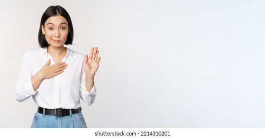 Image of cute young female office worker, asian girl student raising hand up and put palm on chest, name herself, introduce, making promise, standing over white background - Shutterstock ID 2214310201