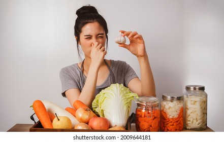 Image of the cuteness of young asian woman prepares the ingredients for kimchi with white garlic as a food ingredient. She feels the pungent smell of her nose. - Shutterstock ID 2009644181