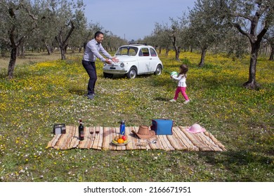 
Image Of A Dad Playing Ball With His Daughter While They Are Having A Picnic During A Vacation In Italy. Background Old Italian Car In A Flowery Field. Italia Lanciano 05-05-2022 