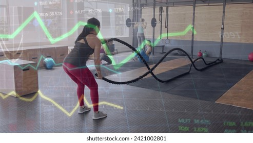 Image of data on graph over caucasian woman cross training with battle ropes at gym. Fitness, exercise, strength, data, digital interface and technology digitally generated image.