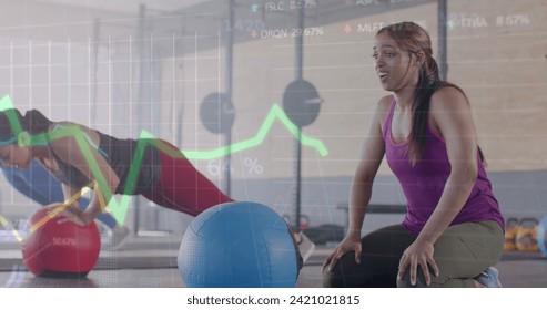 Image of data on graph over diverse women cross training with medicine balls at gym. Fitness, exercise, strength, data, digital interface and technology digitally generated image.