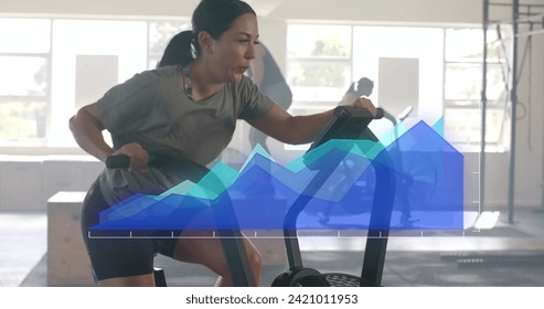Image of data processing on blue graph over caucasian woman cross training on elliptical at gym. Fitness, exercise, strength, data, digital interface and technology digitally generated image.