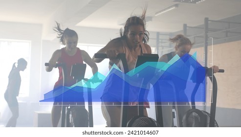 Image of data processing on blue graph over diverse women cross training on ellipticals at gym. Fitness, exercise, strength, data, digital interface and technology digitally generated image.