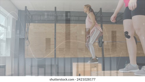 Image of data processing on graph over diverse women jumping on boxes cross training at gym. Fitness, exercise, strength, data, digital interface and technology digitally generated image.