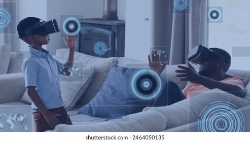 Image of data processing over african american father and son wearing vr headset at home. Fatherhood, love and technology concept - Powered by Shutterstock