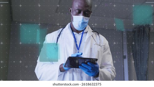 Image of data processing over male african american doctor wearing face mask using tablet. Global covid 19 pandemic, medicine, healthcare and data processing concept digitally generated image.
