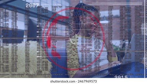 Image of data processing and spinning globe over african american woman using laptop at office. Global networking and business technology concept