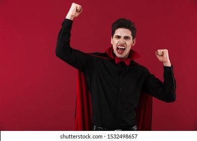 Image Of Delighted Vampire Man With Blood And Fangs In Black Halloween Costume Screaming Isolated Over Red Wall