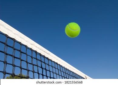 An image depicting the concept of tennis, including a ball gliding over the net in a blue outdoor setting - Powered by Shutterstock