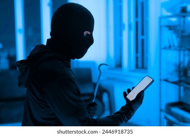 The image depicts a focused thief utilizing a smartphone to aid in a burglary, emphasizing the modern tools used in crime