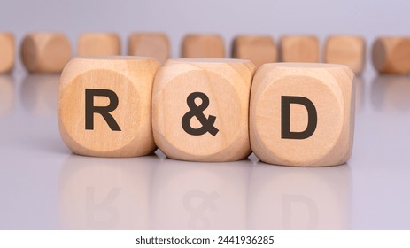 the image depicts three wooden cubes with the letters 'R and D' in focus, reflecting on the table surface. in the background, there is a row of wooden cubes, blurred and out of focus