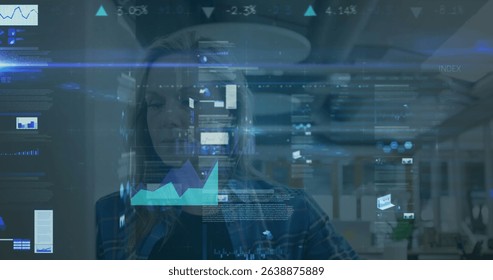 Image of digital business data moving over caucasian businesswoman working in office. Digital composite, business, analysis, multiple exposure, technology, futuristic, planning, occupation.
