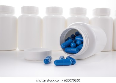 Image displaying a blank white pill bottle, cap off and filled with generic blue capsule pills, laying on its side in front of a line of other blank white pill bottles.