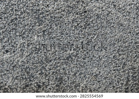 The image displays a close-up view of a stone surface with various textures and shades of gray. The surface features small indentations and uneven areas that create an interesting pattern.