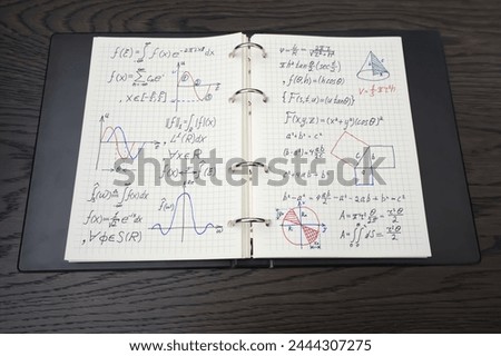 The image displays a notebook filled with complex mathematical equations and colorful graphs, indicative of advanced study in mathematics, placed on a dark wooden surface.
