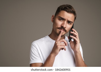 Image of displeased guy showing silence gesture while talking on cellphone isolated over grey background - Shutterstock ID 1842600901
