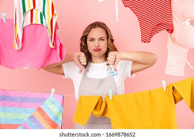 Image Of Displeased Sad Woman Housewife Isolated Over Pink Wall Background Dry Clothes On Rope Showing Thumbs Down.