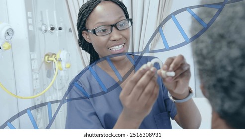 Image of dna strand over african american female doctor fitting hearing aid for senior patient. Check up, data, digital interface, connection, hospital and healthcare, digitally generated image. - Powered by Shutterstock