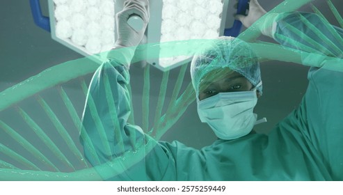 Image of dna strand rotating over african american female surgeon working in theatre. Surgery, digital interface, connection, hospital and healthcare, digitally generated image.