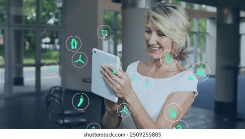 Image of ecology icons over caucasian businesswoman using tablet in office. Business, technology and digital interface concept digitally generated image. - Powered by Shutterstock