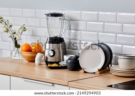 Image of electric blender, set of ceramic plates and other kitchen wares on table in kitchen