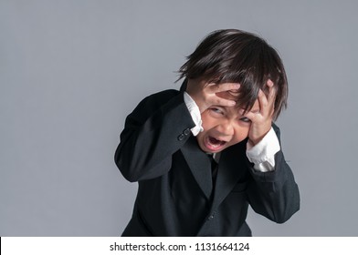 Image of Emotional Disappointment face. Little asian business boy (six years old) with black suit troubling of office syndrome and getting painful feelings and standing while holding his headache.