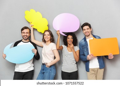 Image of emotional group of friends standing isolated over grey wall background holding speech and thoughtful bubbles.