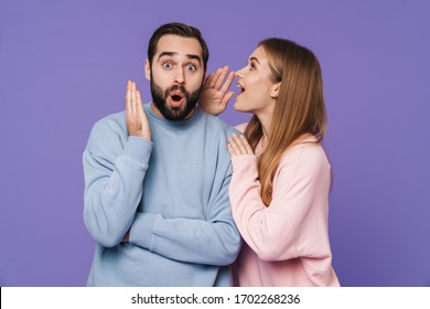Image of emotional surprised young loving couple isolated over purple background gossiping talking with each other.