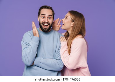 Image of emotional surprised young loving couple isolated over purple background gossiping talking with each other. - Shutterstock ID 1704476563