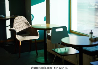 Image of empty seating area in cafe, tables with chairs standing by window in bright sunlight