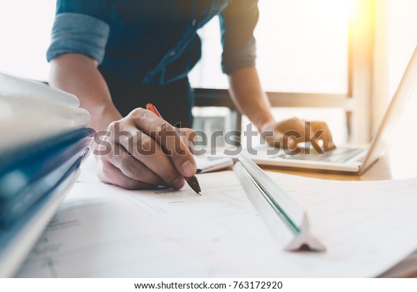 Image of engineer drawing a blue\
print design building or house, An engineer workplace with\
blueprints, pencil, protractor and safety helmet, Industry\
concept