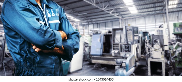 The Image Engineer Men Working In A Manufacturing Plant For Background Of Industry. Men Is Standing With Arms Folded In A Storage Facility Or Warehouse. Men Is Wearing A Uniform Safety Vest.