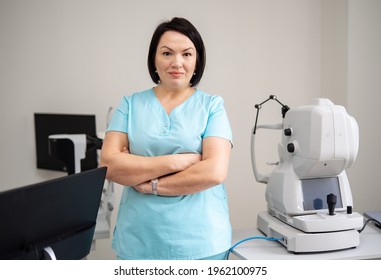 Image Of An Enthusiastic Female Eye Doctor Looking At Camera. Woman Wearing Scrubs On Modern Equipment Background. Closeup.