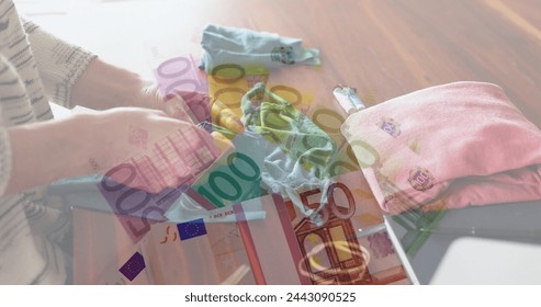 Image of Euro bills lying on a table over Caucasian woman sewing face masks. Coronavirus Covid-19 concept digital composition - Powered by Shutterstock