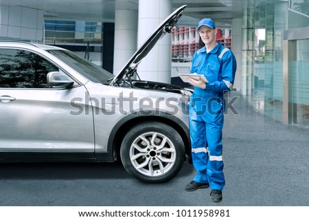 Image of European male mechanic holding a digital tablet while repairing a broken car