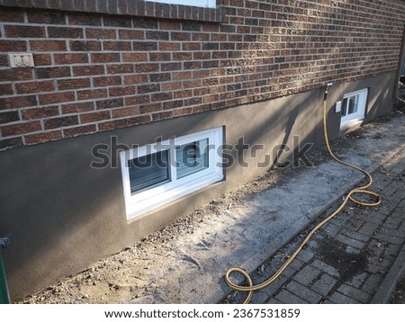 Image example showing a fresh cement exterior parging application layer on foundation wall around two windows with a sandy sponge finish.