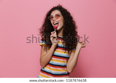 Image of an excited happy cute young woman posing isolated over pink background eat candy lollipop.