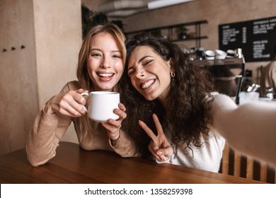 Image of excited happy pretty girls friends sitting in cafe take a selfie by camera. - Powered by Shutterstock