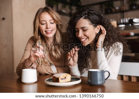 Image of excited happy pretty girls friends sitting in cafe drinking coffee eat cake.