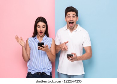 Image of excited man and woman in casual wear holding cell phones isolated over colorful background