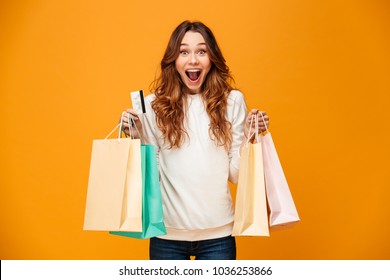 Image of excited screaming young woman standing isolated over yellow background looking camera holding shopping bags and credit card.