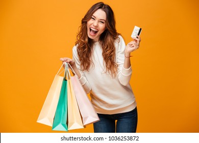 Image of excited screaming young woman standing isolated over yellow background looking camera holding shopping bags and credit card.