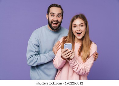 Image of excited surprised loving couple isolated over purple background using mobile phone. - Shutterstock ID 1702268512
