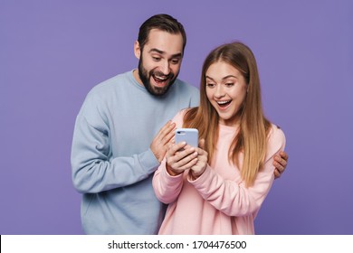 Image of excited surprised loving couple isolated over purple background using mobile phone.