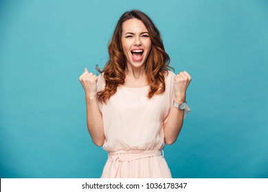 Image of excited young lady standing isolated over blue background make winner gesture.