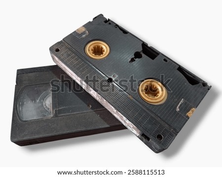 The image features a black rectangular object that resembles an old video cassette.It has a round metal object positioned on top of it.This cassette is related to electronics and data storage devices.