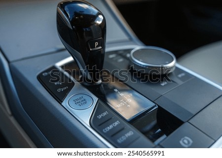The image features a close up of a BMW gear shift with a sleek black finish, surrounded by control buttons including Start or Stop Engine and driving modes.